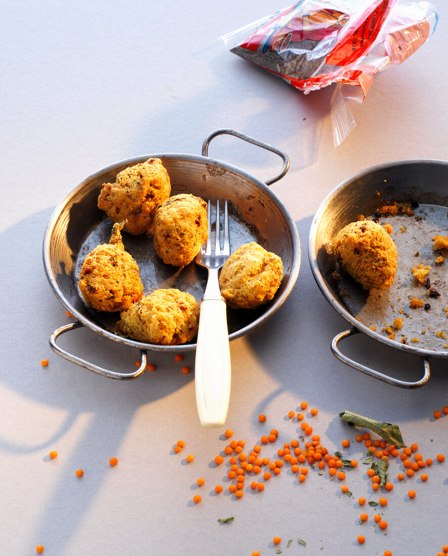 Red lentil balls with fork in small flat woks