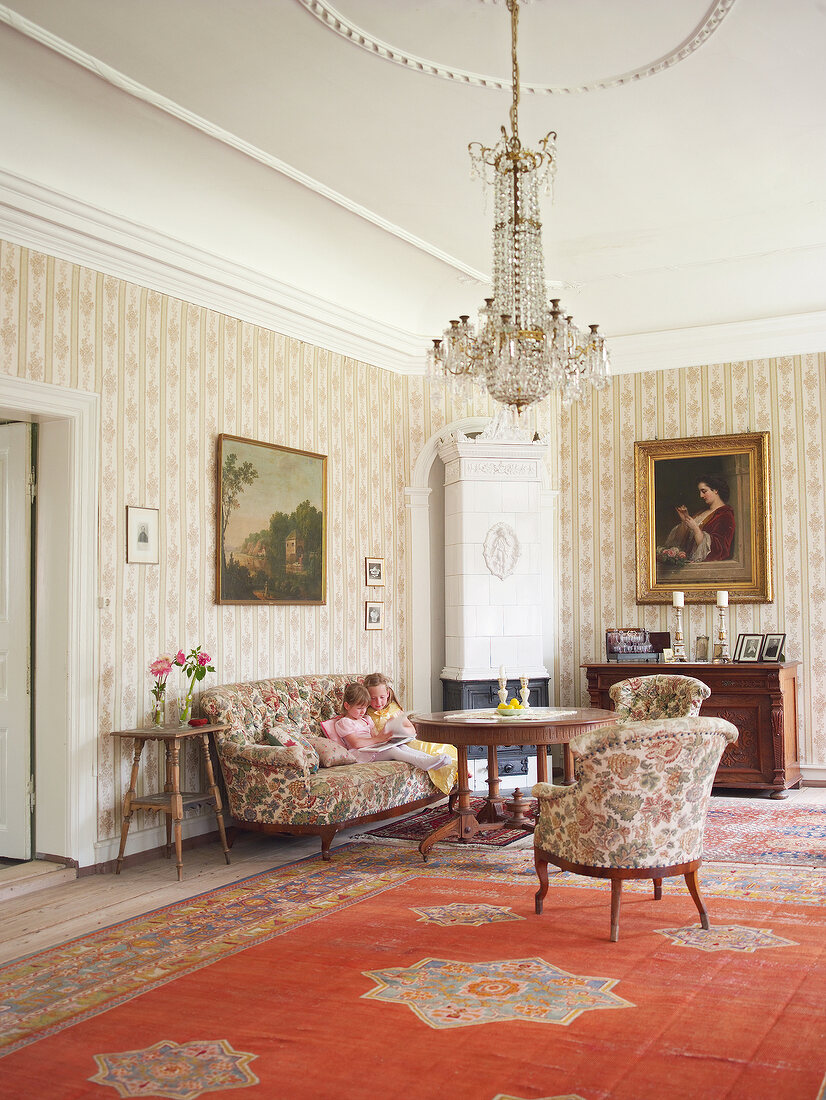 Two girls sitting on sofa in lounge with chandelier and carpet in Rieseby, Germany