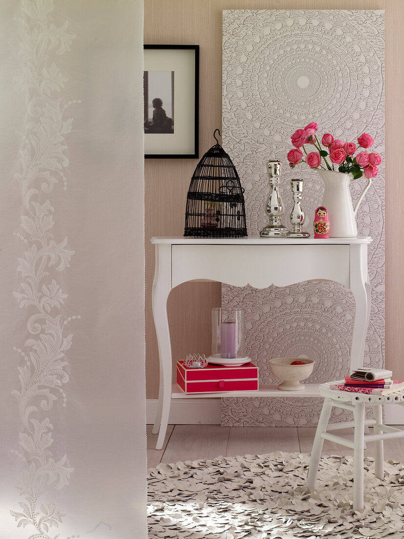 Console table with flower vase and cage against white lace patterned wallpaper