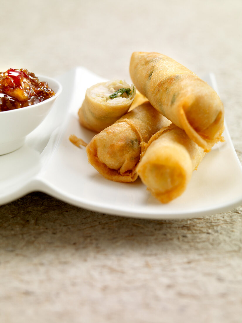 Close-up of four spring rolls on plate with fig sauce in bowl