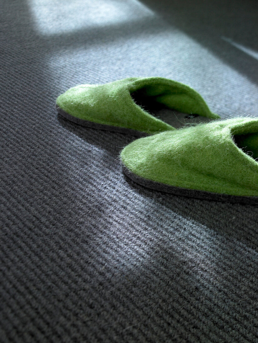 Pair of green felt slippers on grey carpet