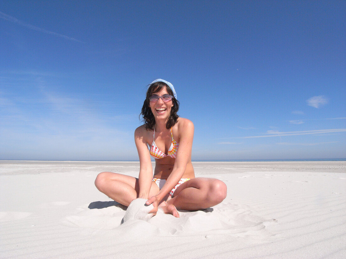 Woman wearing bikini playing with sand on beach, smiling