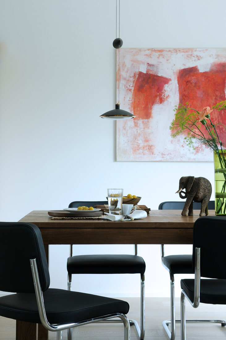 Wooden table with black chairs in front of painting on white wall in dining area