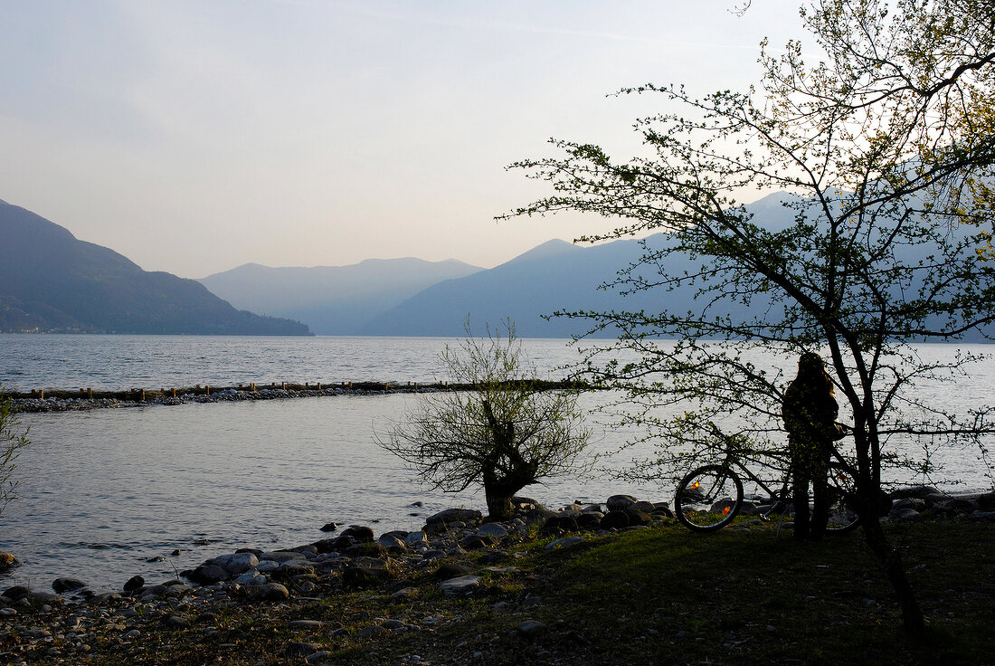 View of man with cycle at Ascona mountain range and lake at dusk in Ticino, Switzerland