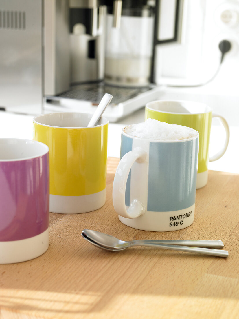 Four coffee mugs from pantone with spoons on wooden board