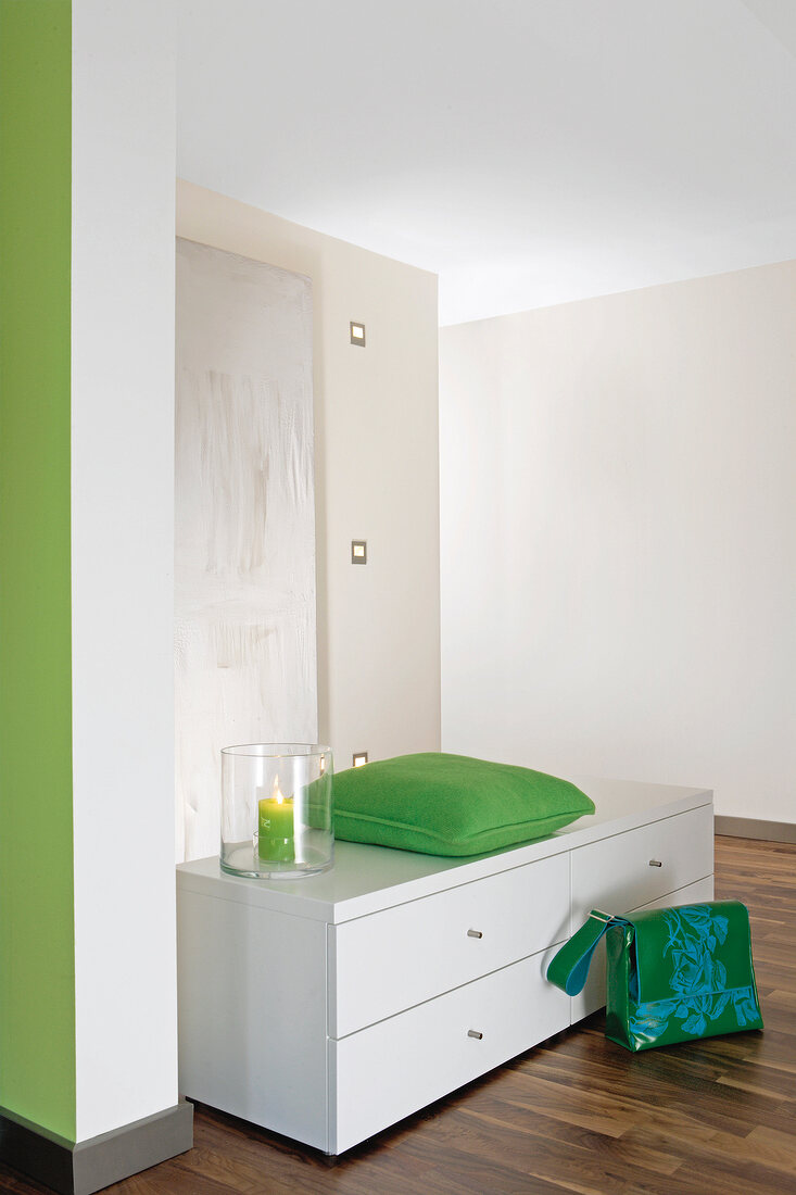 Green cushion on white chest of drawers in corridor