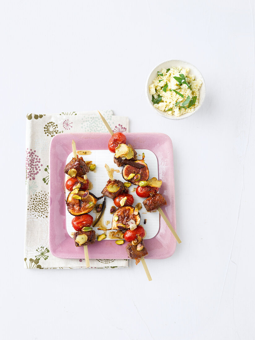 Lamb skewers with cherry tomatoes, figs and pistachio marinade on plate, overhead view