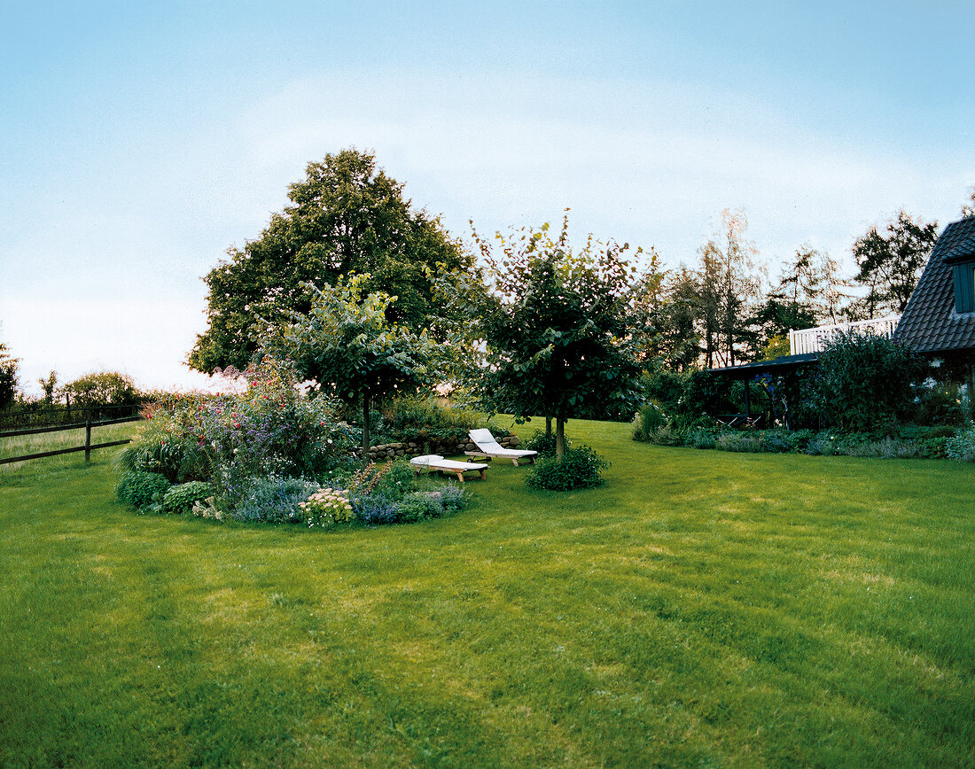 View of garden with trees, shrubs, lawn, flowers and two chairs