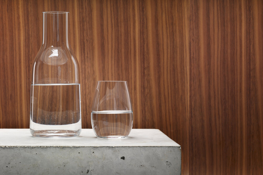 Water in glass and bottle on table against brown background