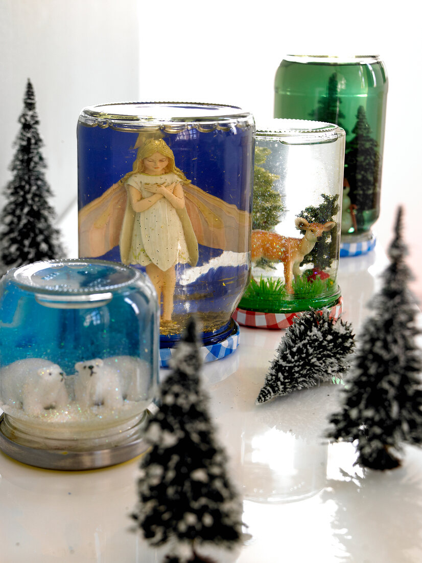Figurines in upside down glass jars as homemade snow globes decorated with glitter