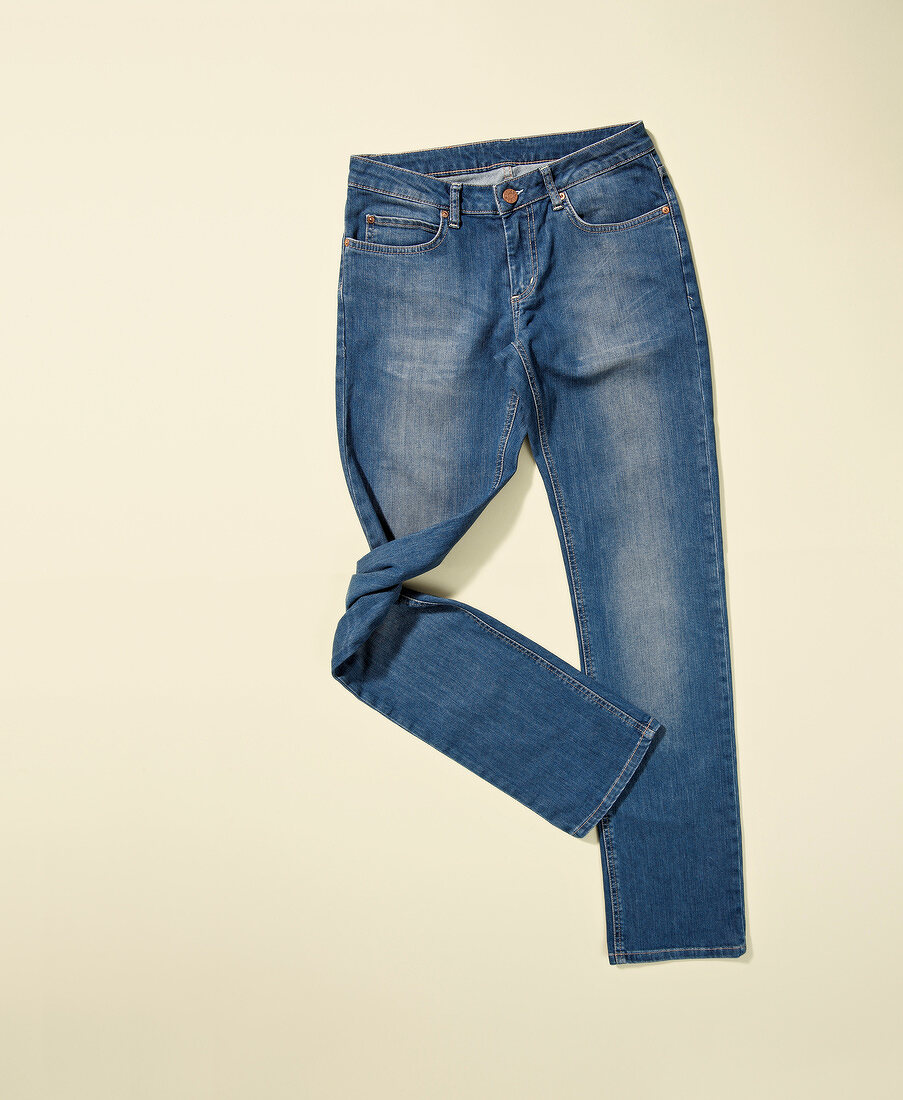 Blue jeans with twisted leg on cream coloured background