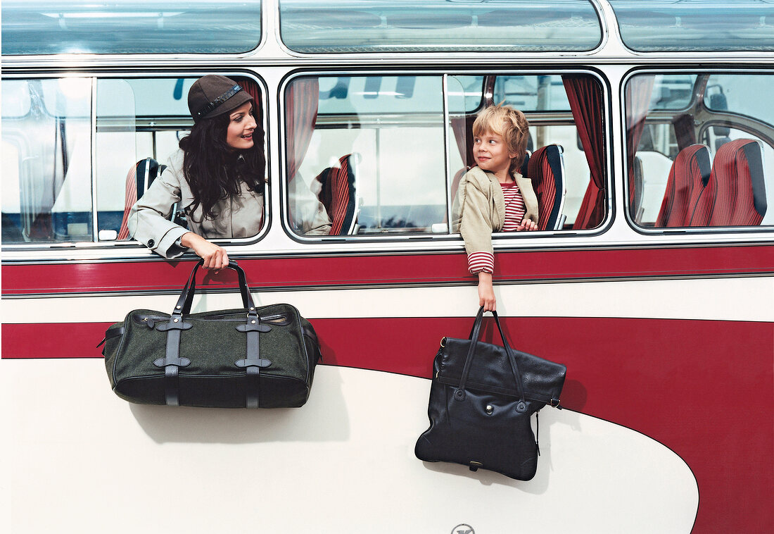 Woman and child holding travel bags out of bus window, smiling while looking at each other