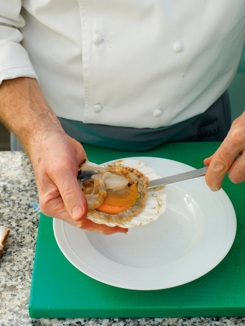 Close-up of man's hands removing mussel meat from shell with knife