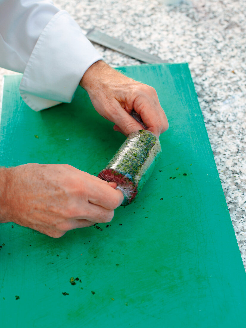 Man's hands sealing ends of cling film with screw beef in it