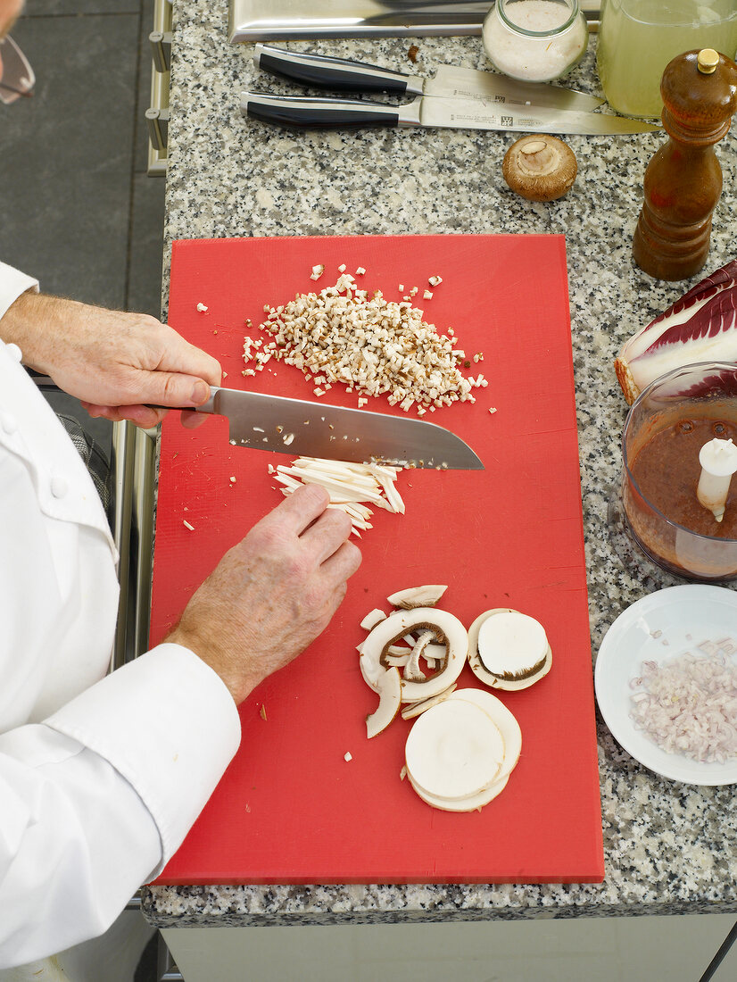 Man's hands chopping mushrooms with knife on cutting board