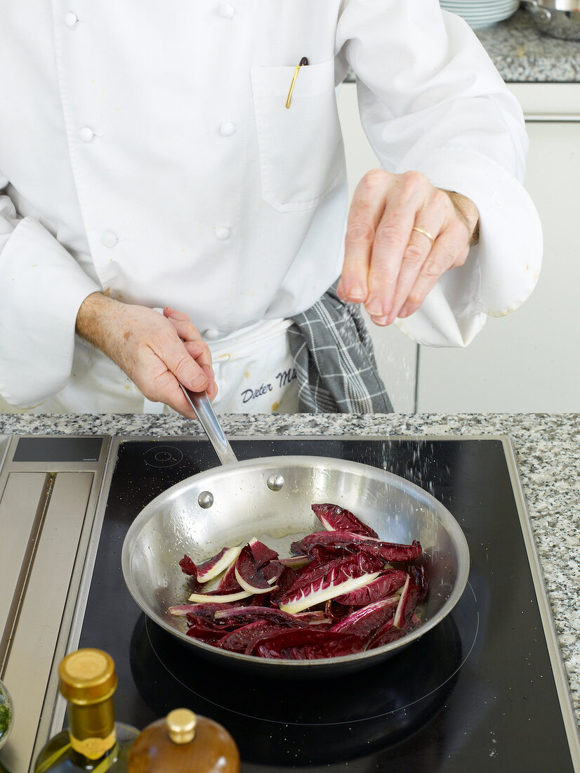 Man's hand seasoning roasted chicory with salt and pepper