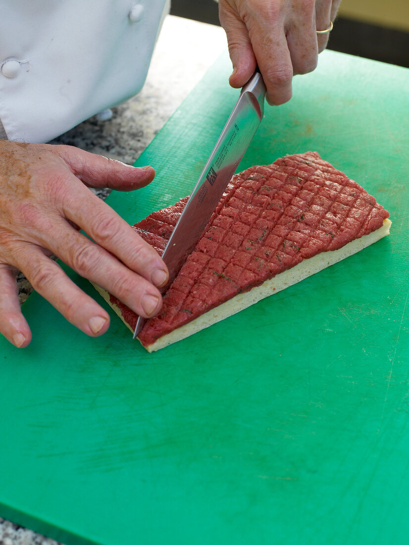 Focaccia bread tatar being cut in lattice pattern with knife on cutting board
