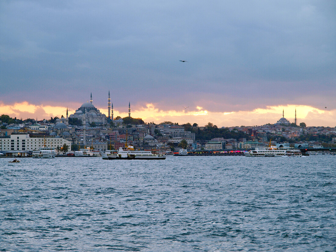 View of cityscape of city on coast of Bosphorus and ferryboats at dusk, Istanbul, Turkey