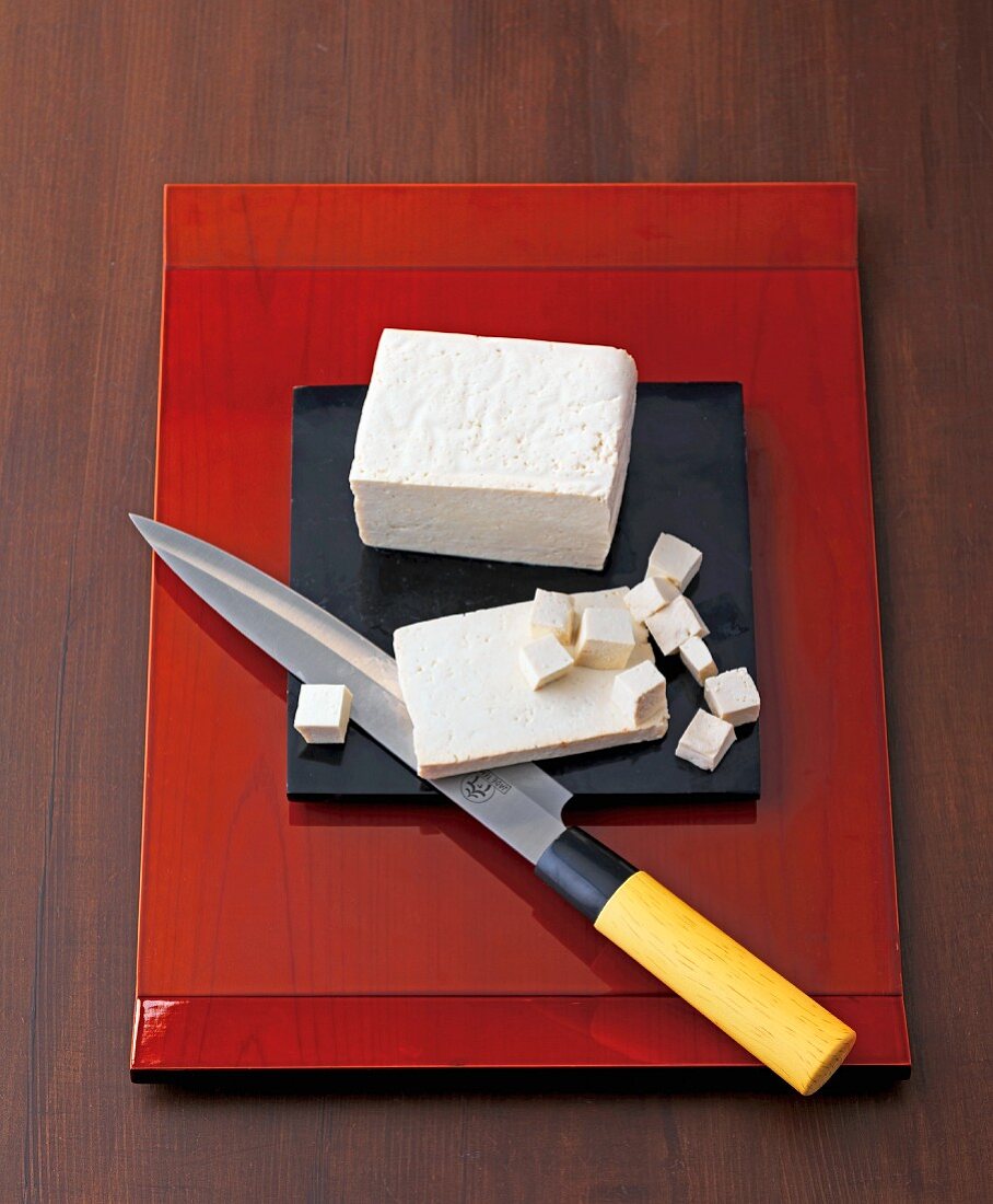 Ein Block Tofu in Scheiben & Würfeln mit Messer auf Schneidebrett