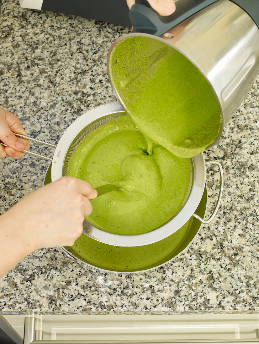 Green puree being strained with strainer