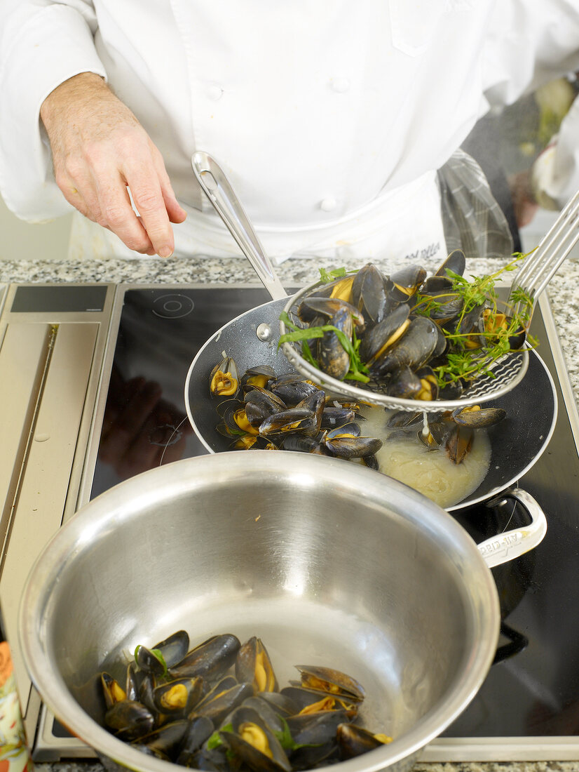 Close-up of man's hands removing bouchot mussels with strainer spoon from pan