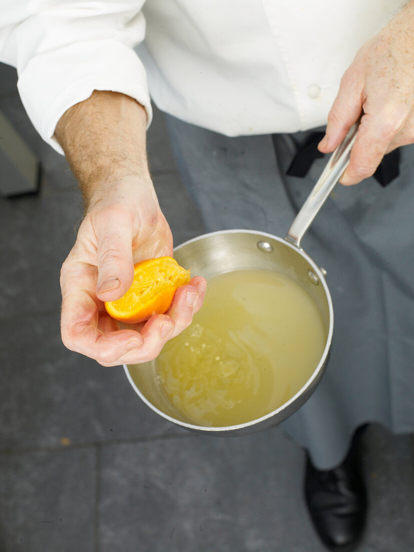 Close-up of man's hands squeezing orange in pan