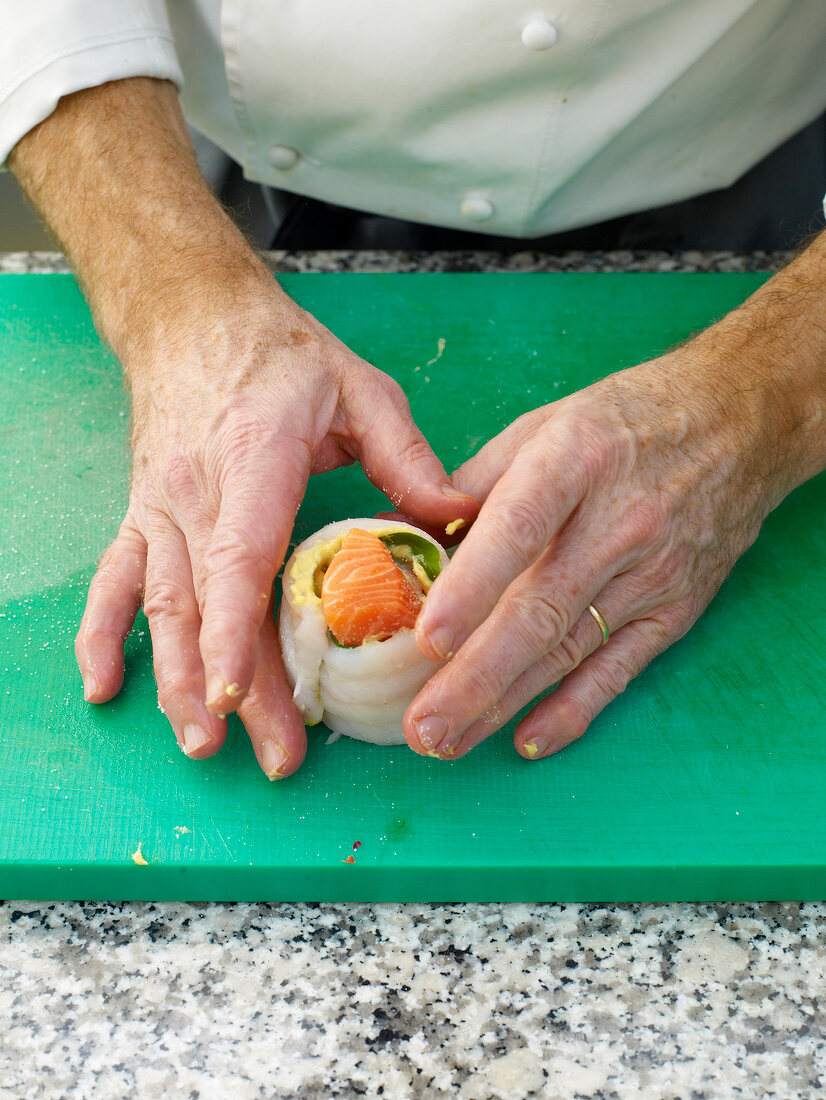 Close-up of man's hands wrapping sole on cutting board
