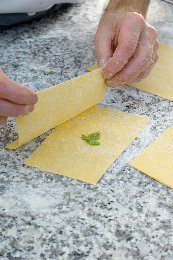 Close-up of man's hands holding pasta sheet and placing on other pasta sheet