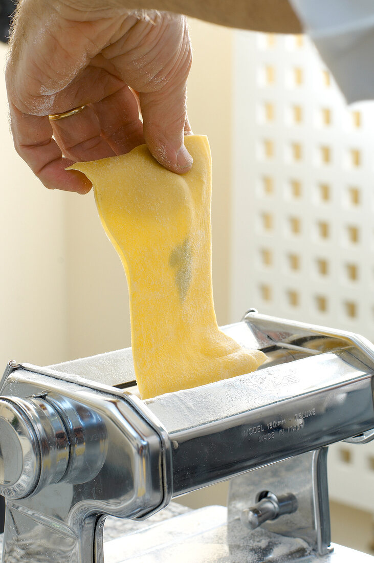 Close-up of man's hand preparing pasta sheet on machine