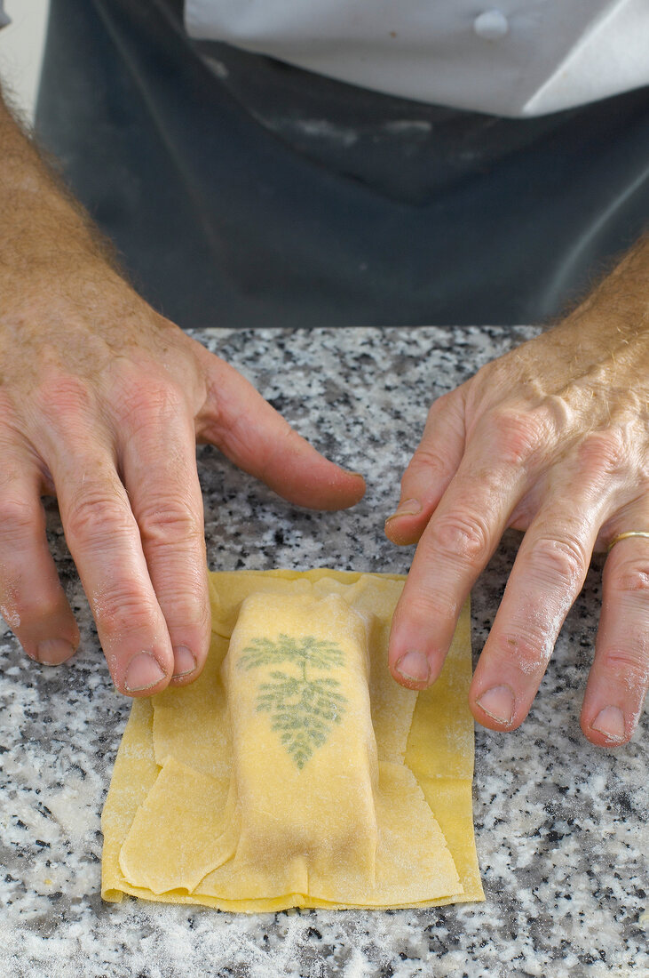 Close-up of man's hand covering pasta dough with chervil leaf and salmon fillet