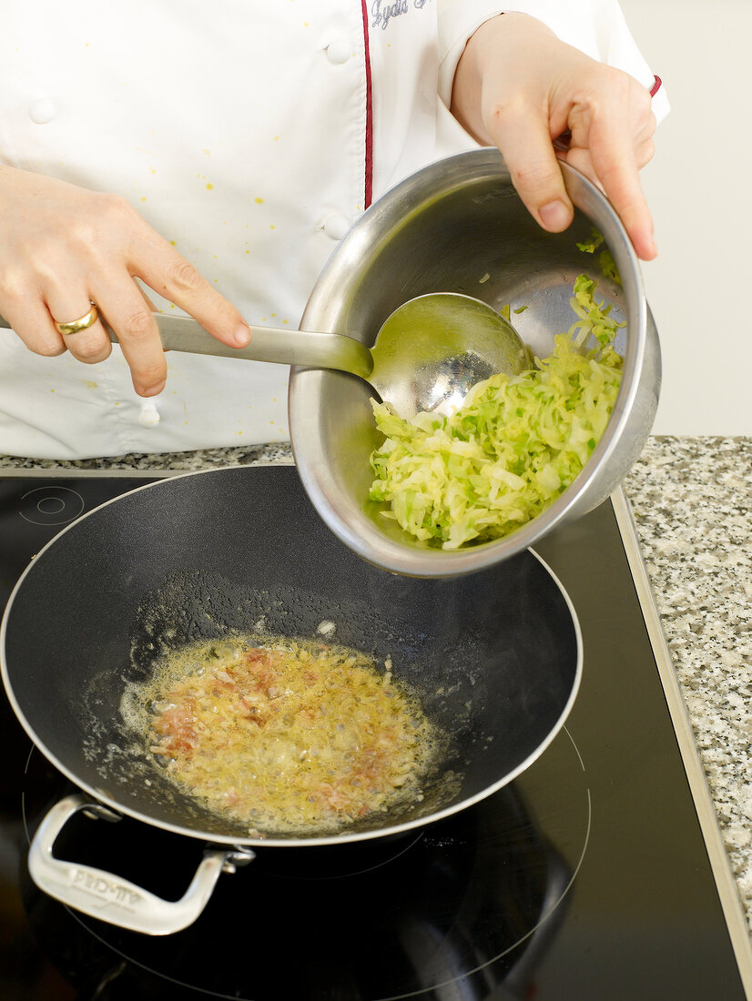 Sliced cabbage being mixed with paste in cooking pan