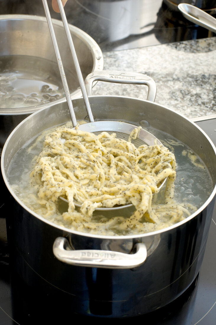 Removing poppy noodles from boiling water with strainer