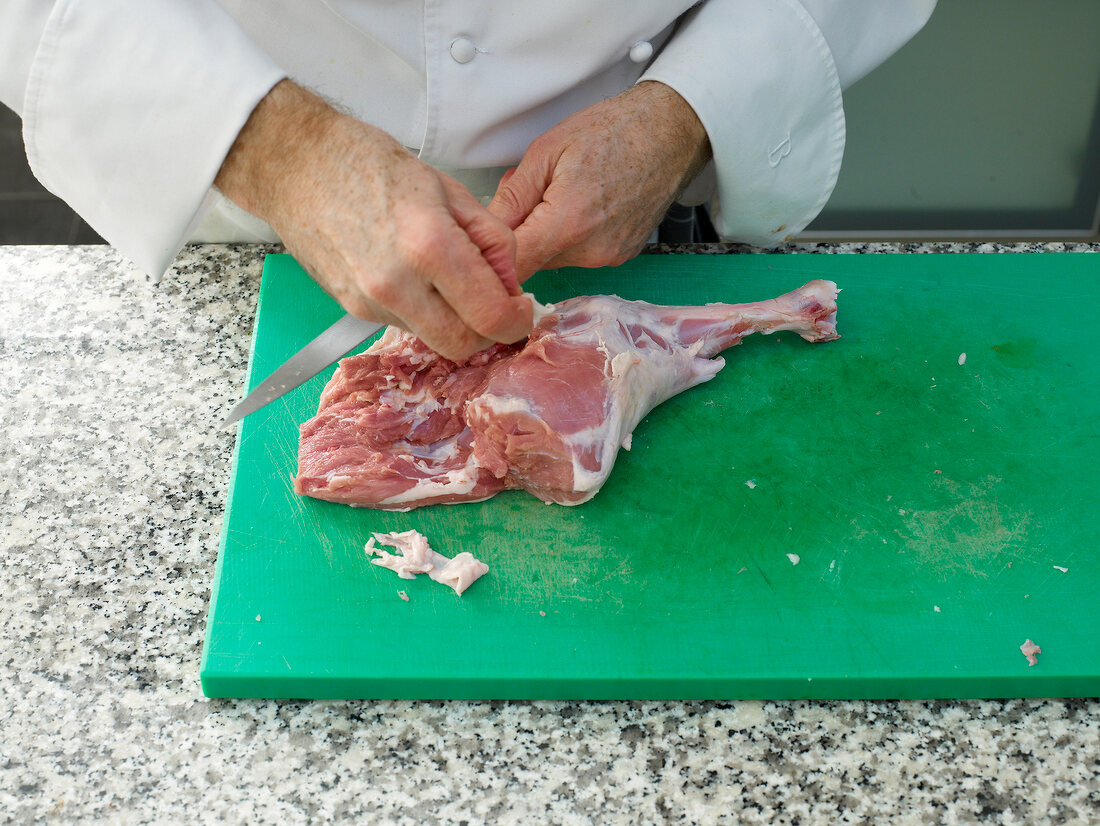 Chef cutting lamb's leg with knife