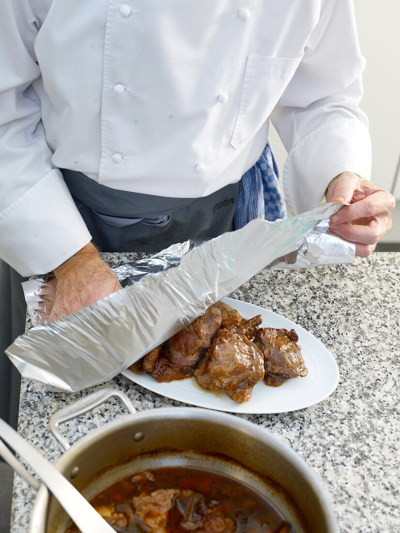 Aluminium foil being wrapped over veal cheeks on serving dish