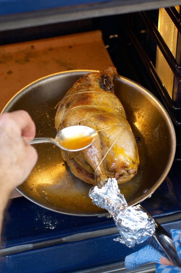 Pouring oil with a spoon on stuffed pheasant in frying pan