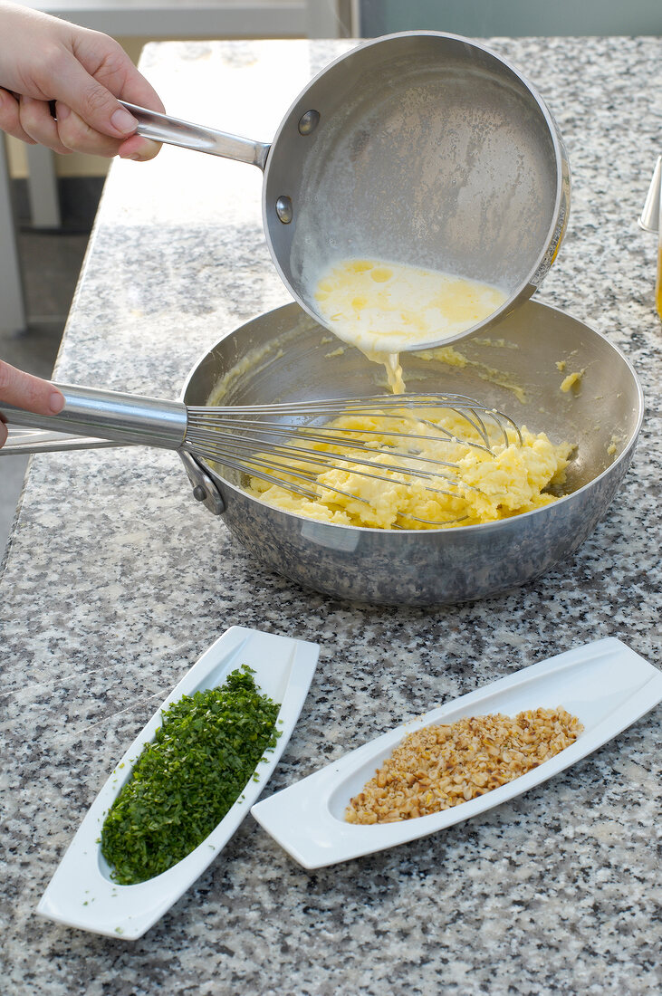 Pouring milk mixer in mashed potatoes and whisking