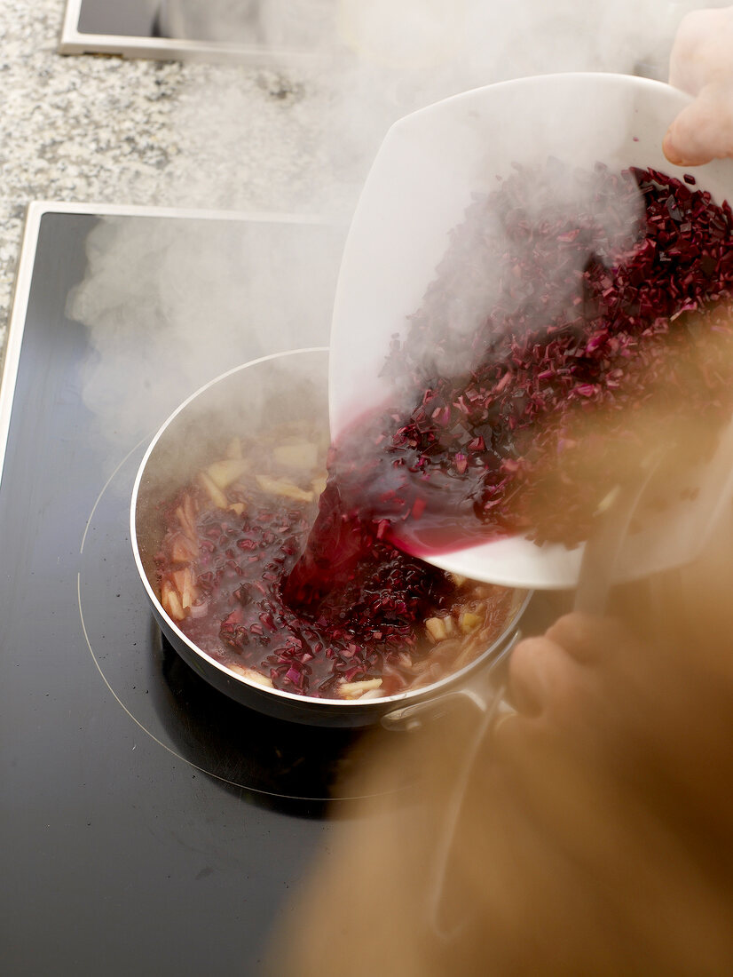 Mixing red cabbage in saucepan with apple pieces