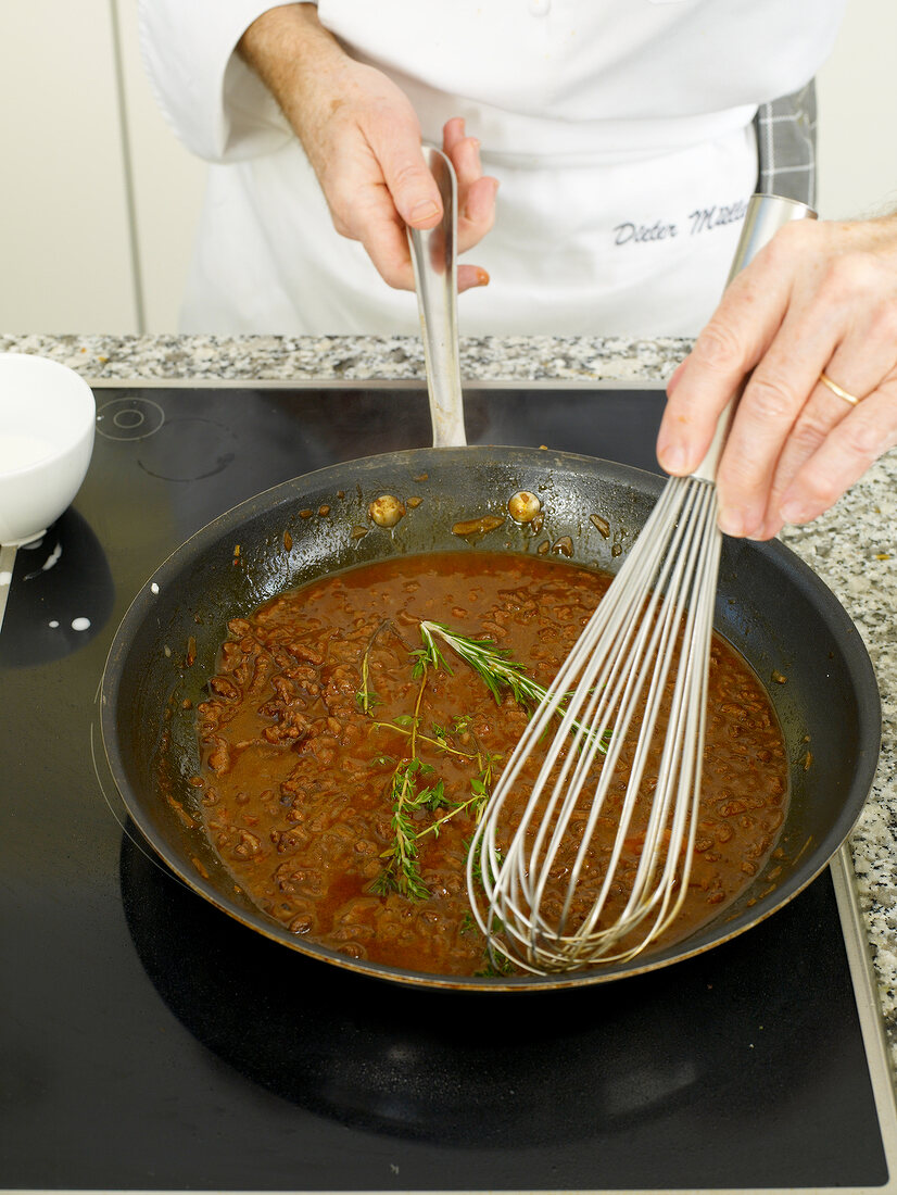 Mixing partially cooked sauce with whisk in frying pan
