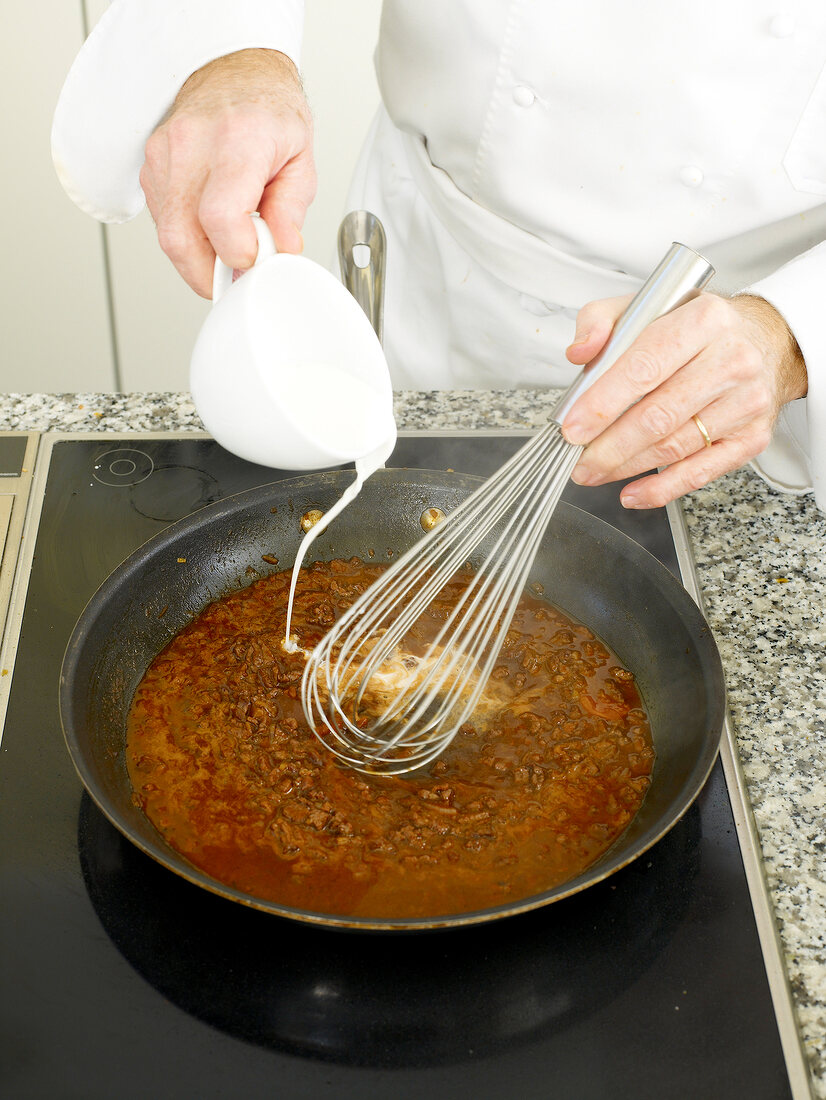 Adding milk to ingredients of beef sauce in frying pan