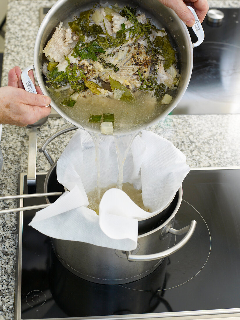 Straining fish stock mixture with mesh sieve in pot