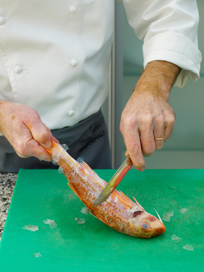 Removing skin of red mullet by knife on chopping board