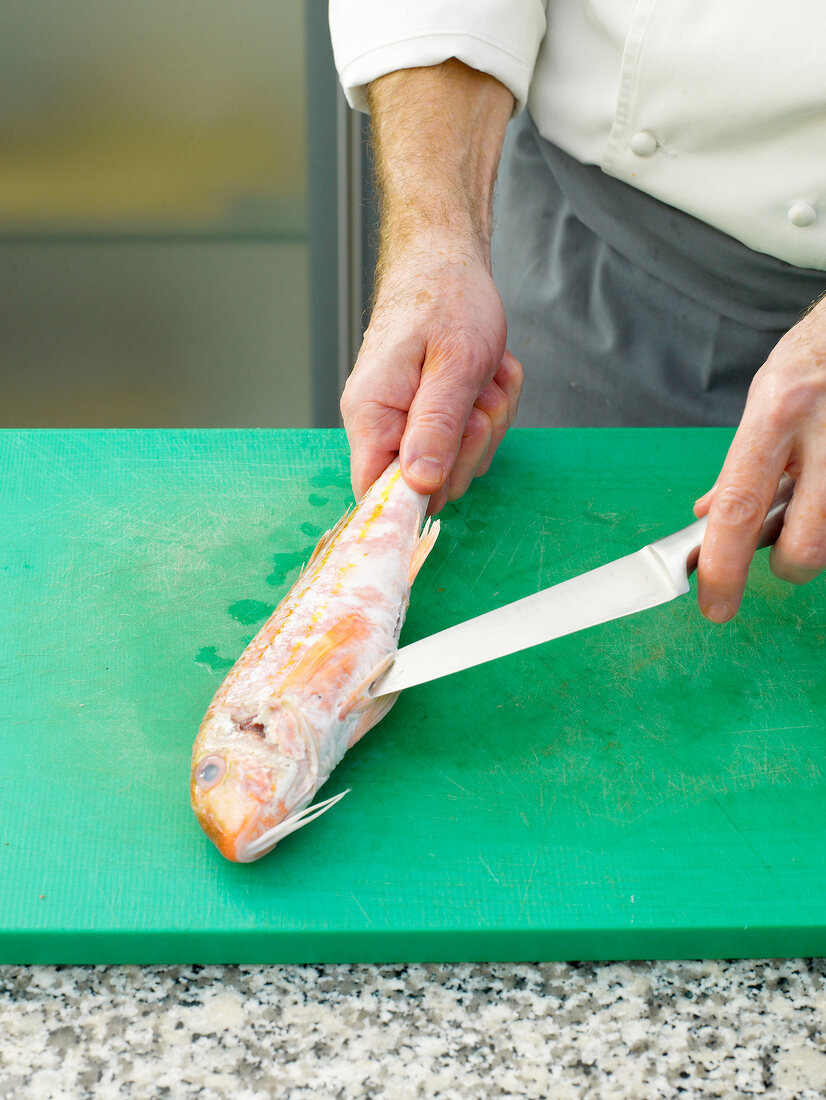 Slicing red mullet by knife on chopping board