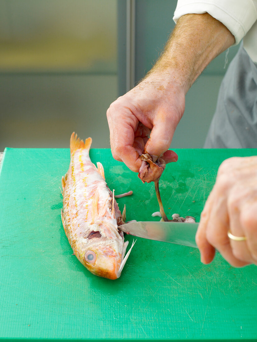 Removing gizards of red mullet by knife on chopping board