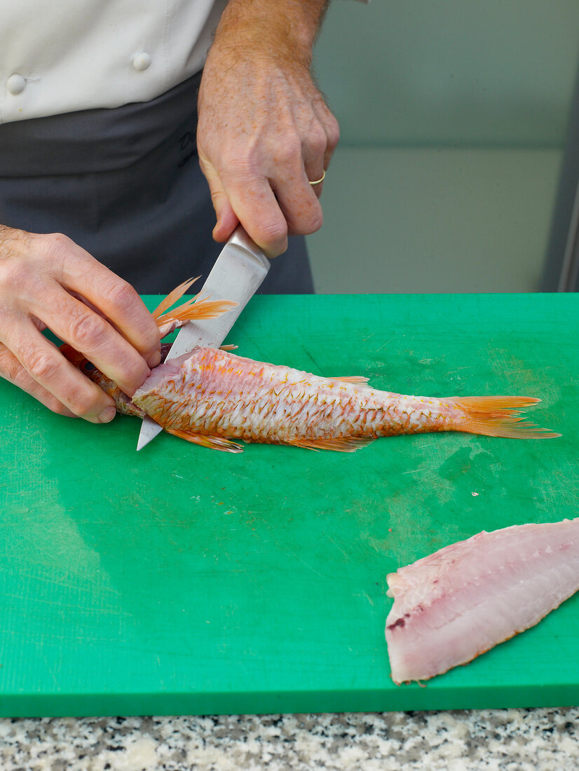 Filleting red mullet by knife on chopping board