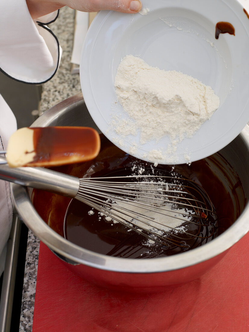 Adding flour to chocolate in bowl with whisk