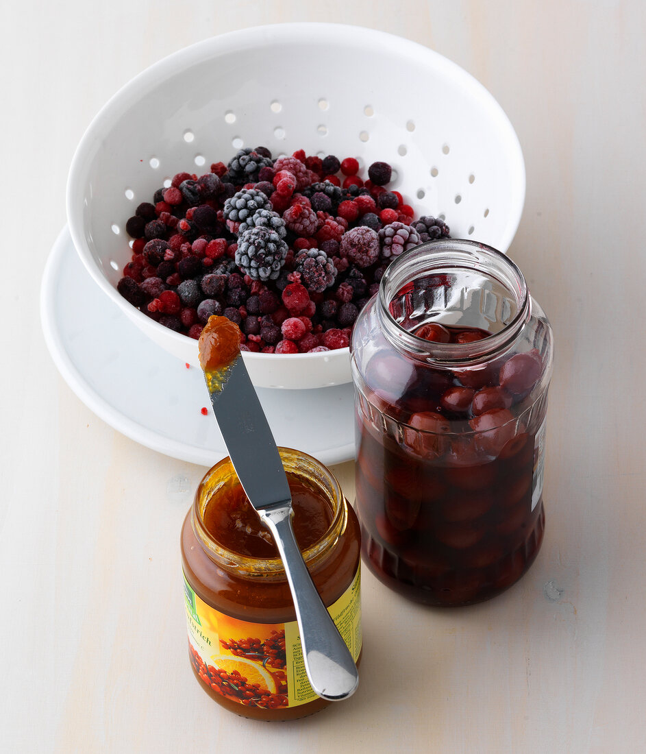 Bowl of different berries and jars of berry products