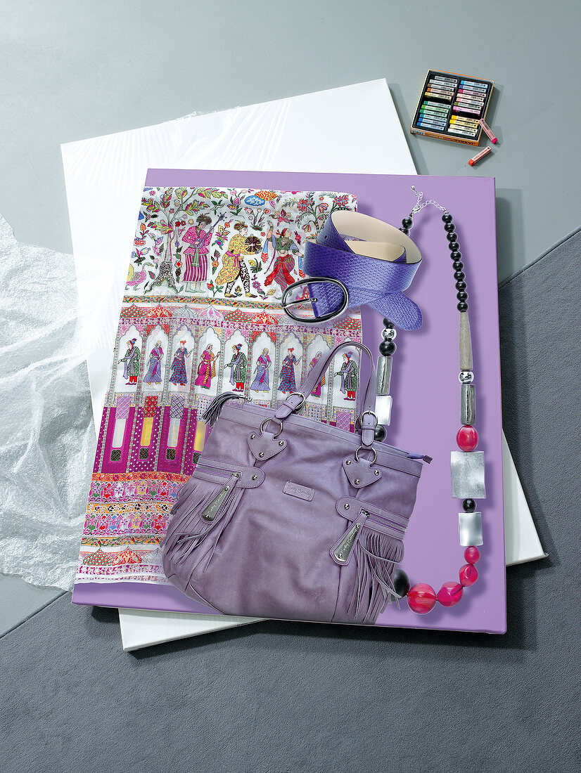 Close-up of purple scarf, belt, bag, ball chain on gray background