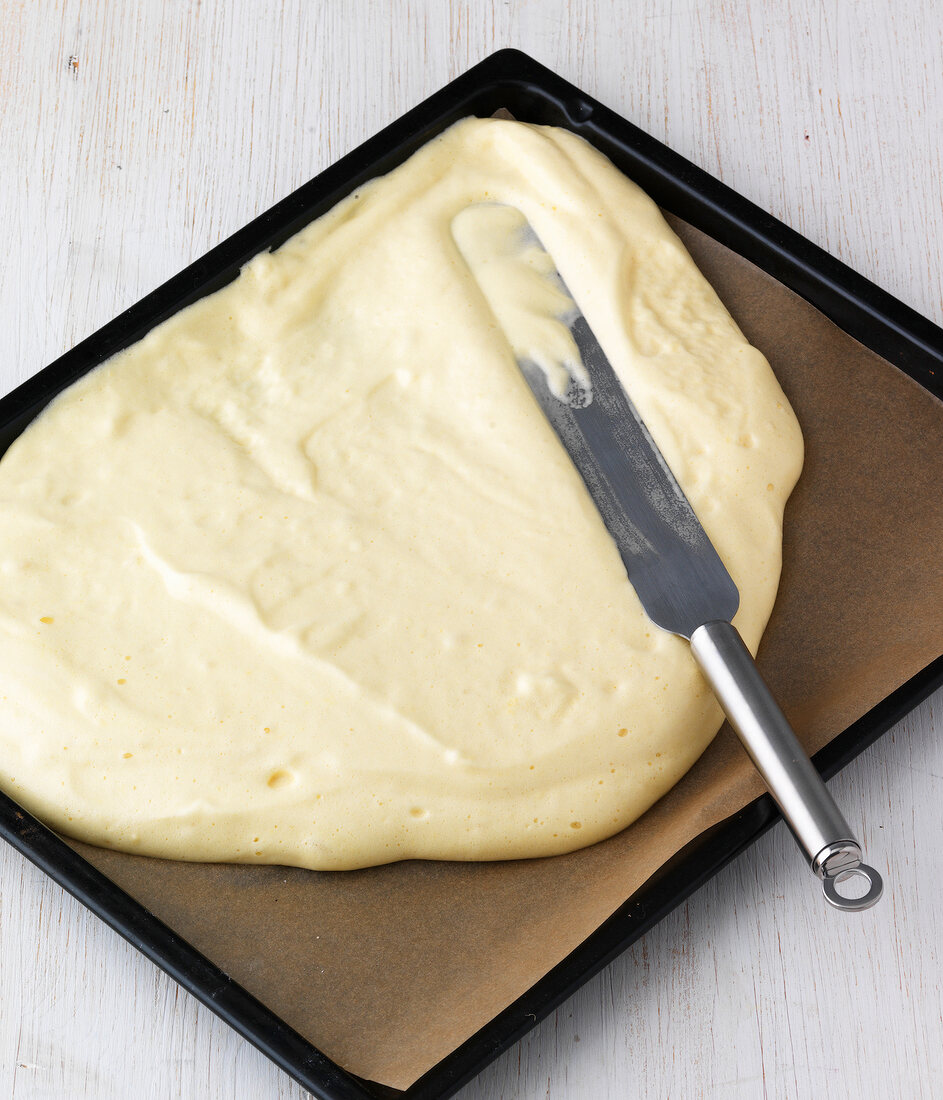 Spreading mixture with spatula on baking tray for preparation of lemon roll, step 1