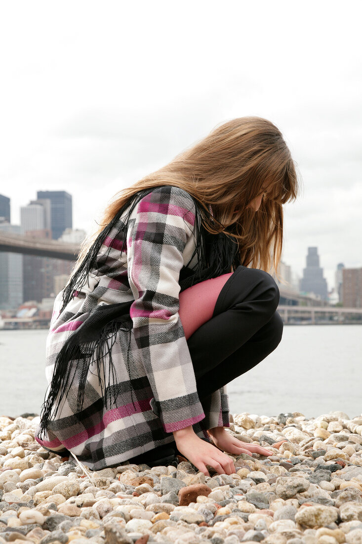 Side view of brunette woman wearing plaid outfit, crouching and looking down