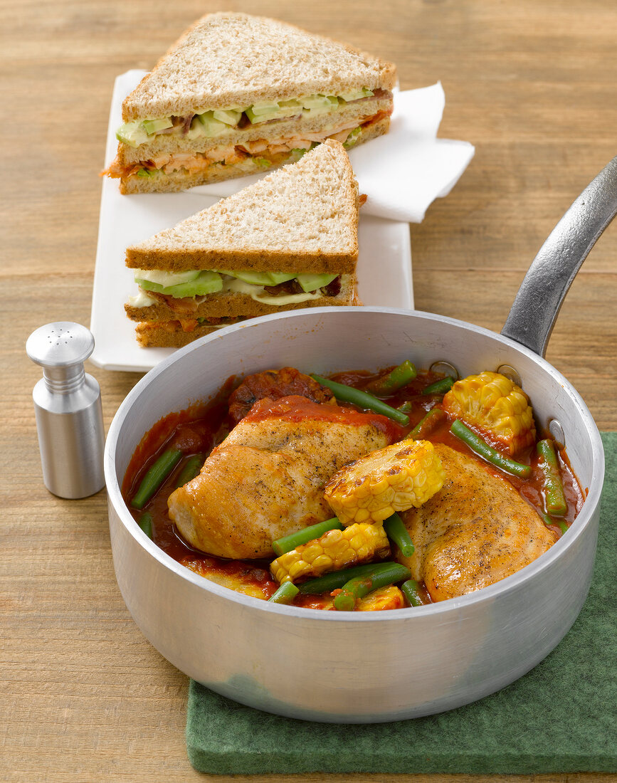 Braised chicken with corn in pan and club sandwich on plate